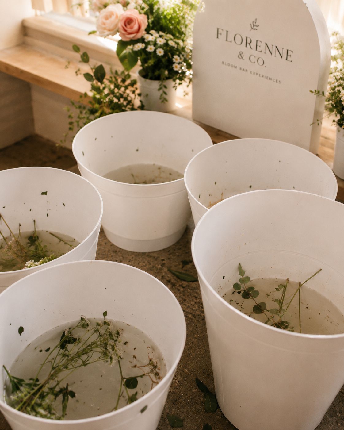 White flower buckets being emptied and refreshed behind the scenes, with the Florenne & Co. sign in the background