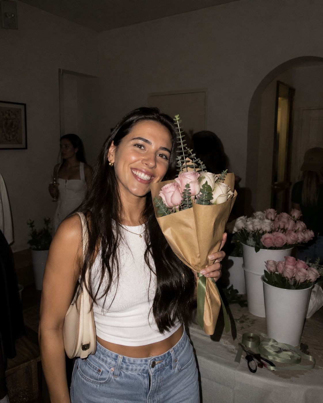 A smiling guest holding her kraft-wrapped bouquet of roses at an evening celebration