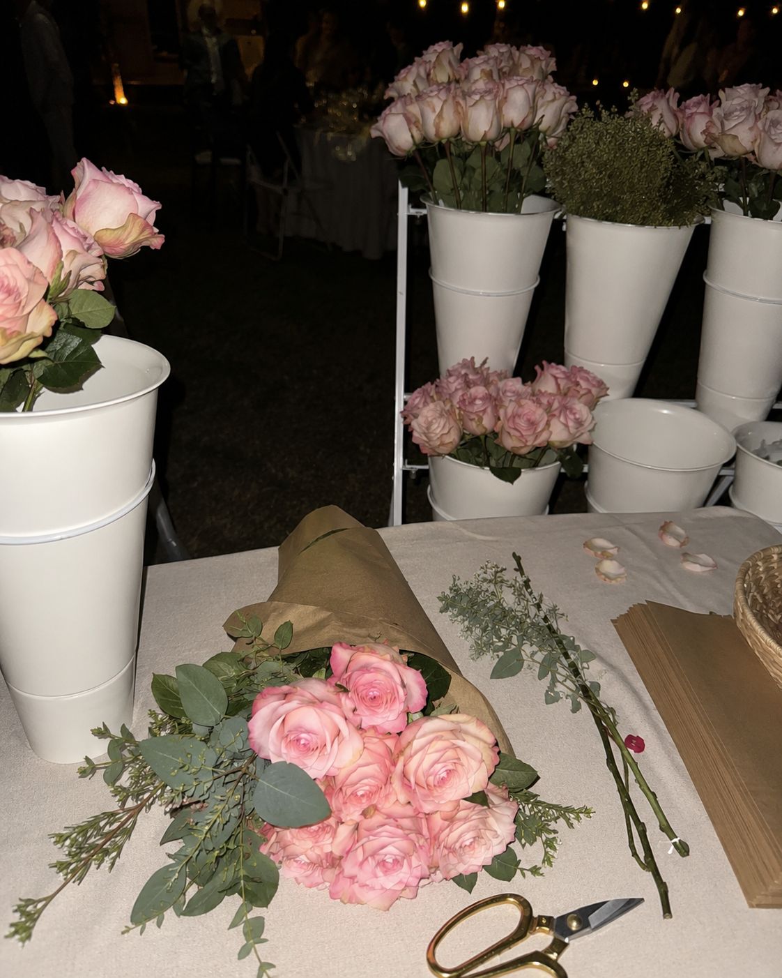 A finished bouquet of pink roses wrapped in kraft paper on the flower bar table at an evening event