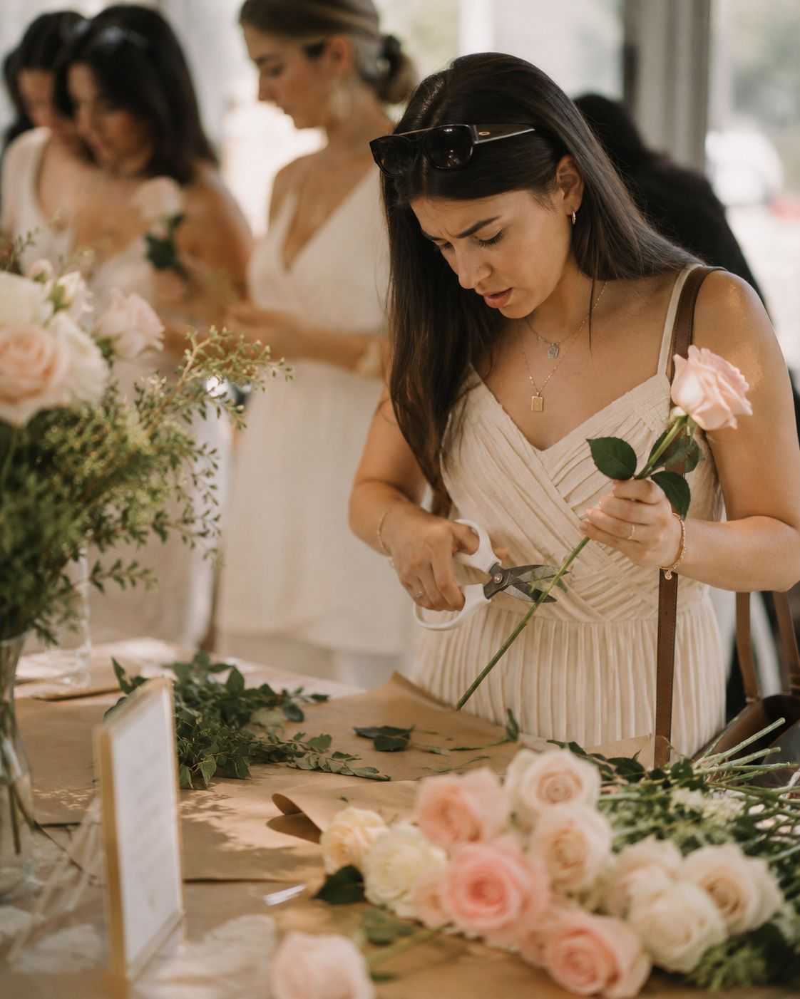 A guest in a cream dress trimming a rose stem with floristry scissors during a bloom bar event